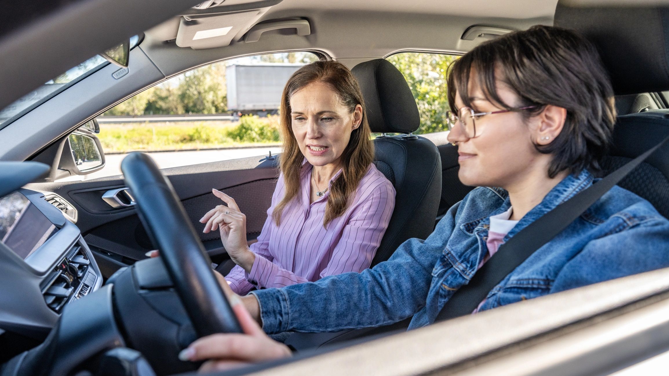 Female driving instructor guiding a student during a driving lesson.